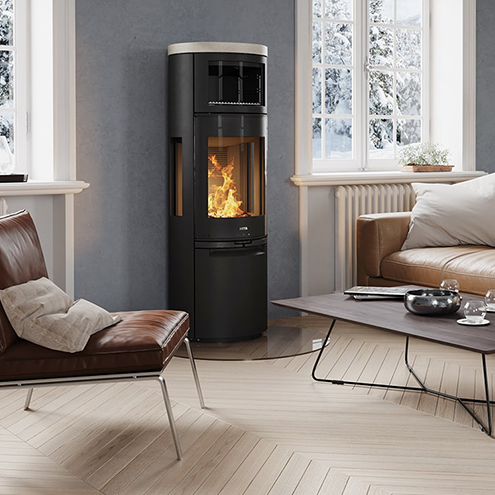 Aska från Kamin: En komplett guide till säker hantering 4 Ett modernt vardagsrum med en brun läderfåtölj, en svart vedspis med synliga lågor, ett lågt soffbord och stora fönster som visar ett snöigt landskap utanför.