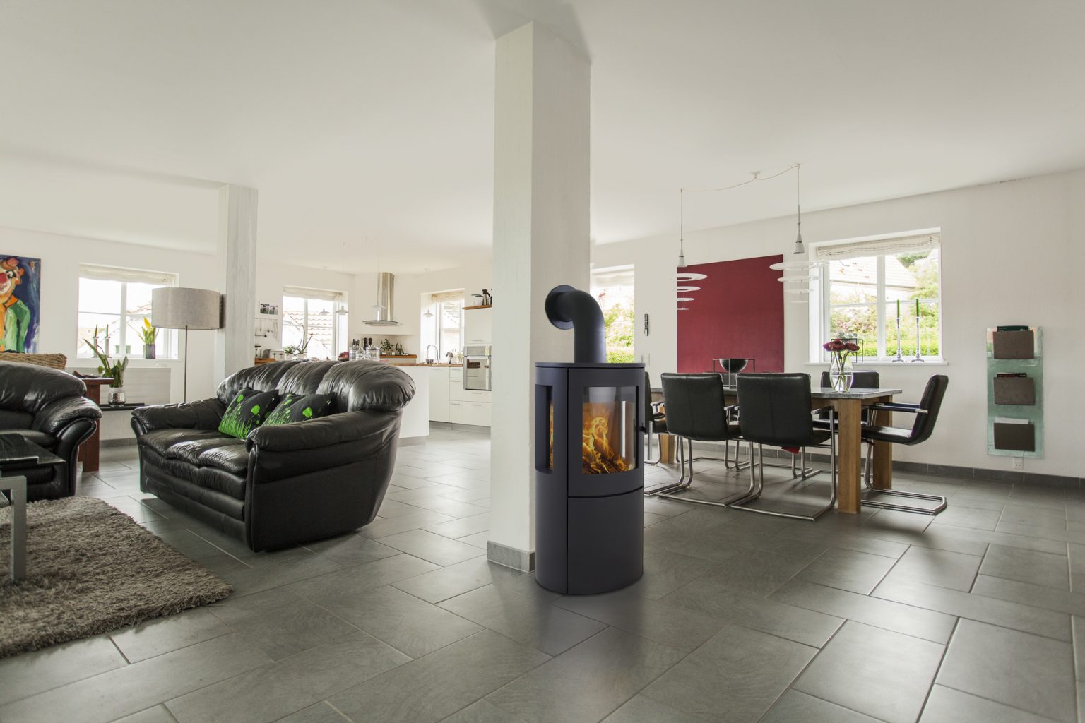 Modernt vardagsrum och matplats i öppen planlösning med svarta skinnsoffor, fristående braskamin, matbord med svarta stolar, stora fönster och klinkergolv.