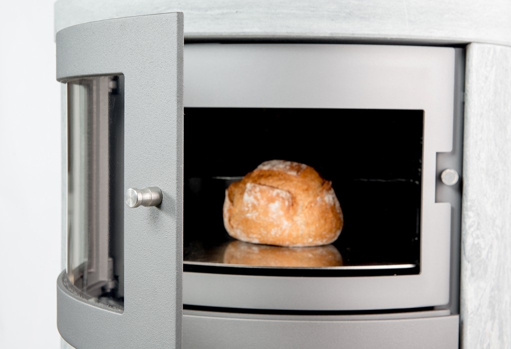 En limpa bröd bakas i en modern kamin med ugn i metall, med dörren något öppen, vilket avslöjar brödet på en mörk ugnsplåt.