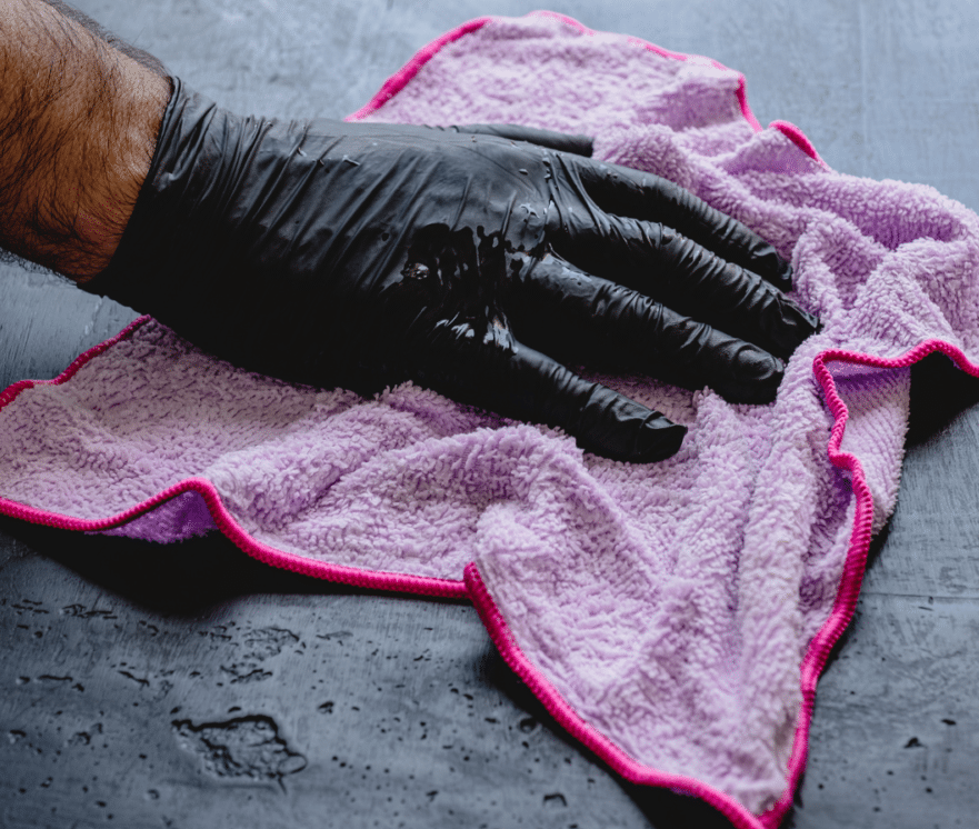 En person med svart handske torkar av en våt yta med en rosa mikrofiberduk, perfekt för att rengöra täljsten.