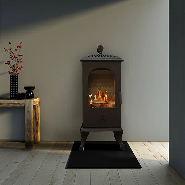 En svart kamin kokplatta med glasdörr och synliga lågor står på en svart matta i ett modernt rum med ljust trägolv. Ett rustikt träbord med minimalistisk inredning står till vänster mot väggen.