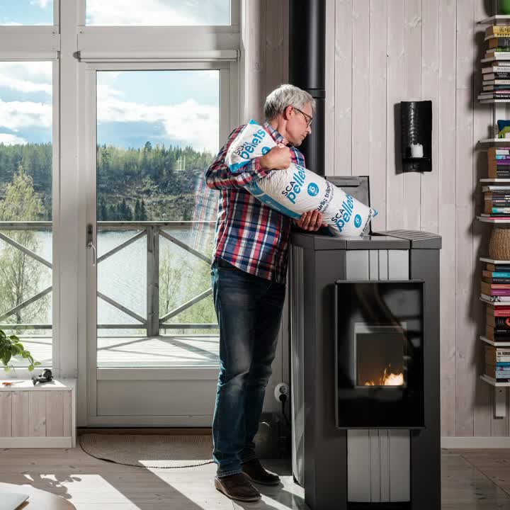 En man står upp med en pelletspåse och häller ner det i kaminen.