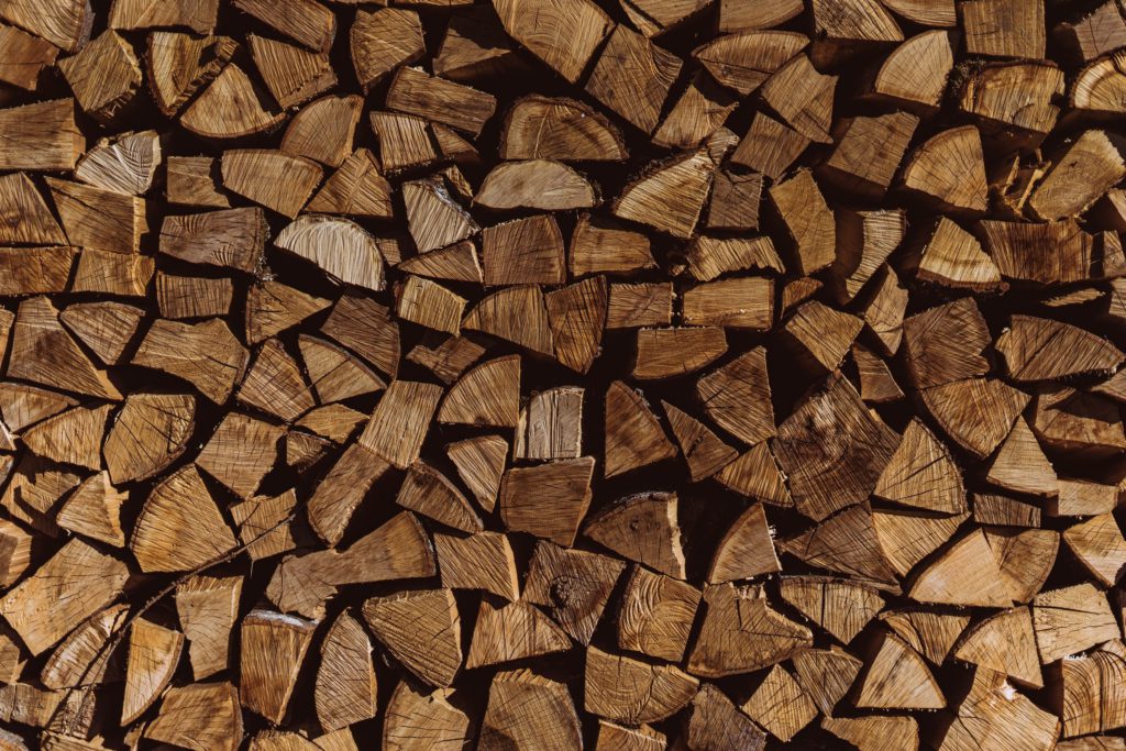 Staplar av hackad ved, arrangerade i ett tätt packat mönster med synliga trädringar och varierande nyanser av brunt, skapar en rustik textur.