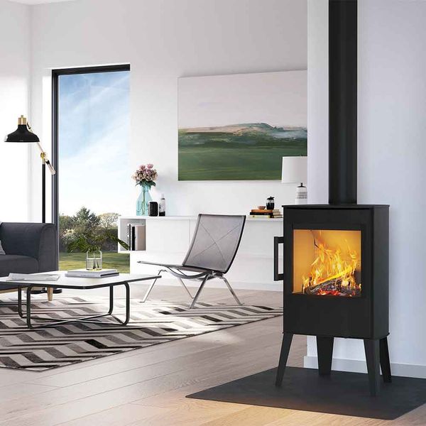 Ett modernt vardagsrum med en liten kamin, randig matta, minimalistiskt soffbord, fåtölj och stora fönster med utsikt över ett grönt utomhuslandskap.