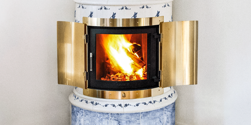 Gabriel Kakelugnar: En guide till svenska klassiker 2 En mässingsklädd öppen spis med öppna dörrar visar en brinnande eld inuti. Den öppna spisen är placerad i en struktur av vitt och blått kakel med ett dekorativt mönster.