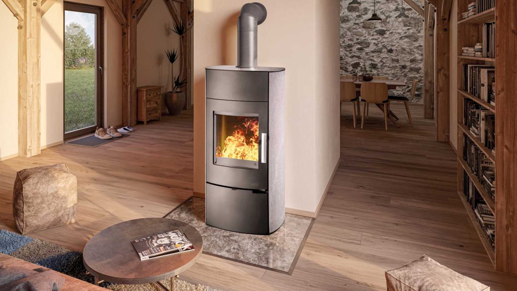 En modern braskamin med synlig låga står i ett mysigt vardagsrum, omgivet av trägolv, bokhyllor och rustik inredning. Ljuset flödar in från en glasdörr och en matplats syns i bakgrunden.