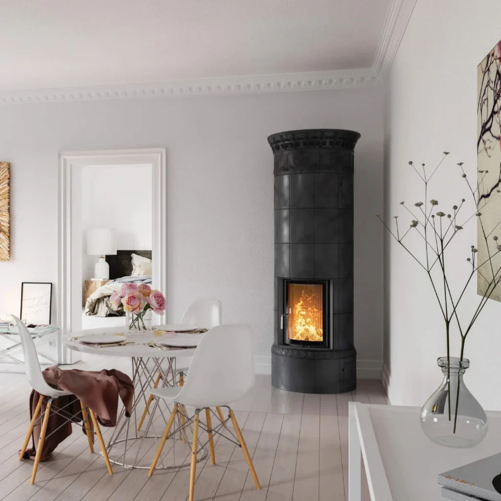 En modern matsal med ett runt vitt bord, fyra vita stolar, en vas med blommor och en hög svart cylindrisk öppen spis med en synlig eld som brinner, mot vita väggar och ljust trägolv.