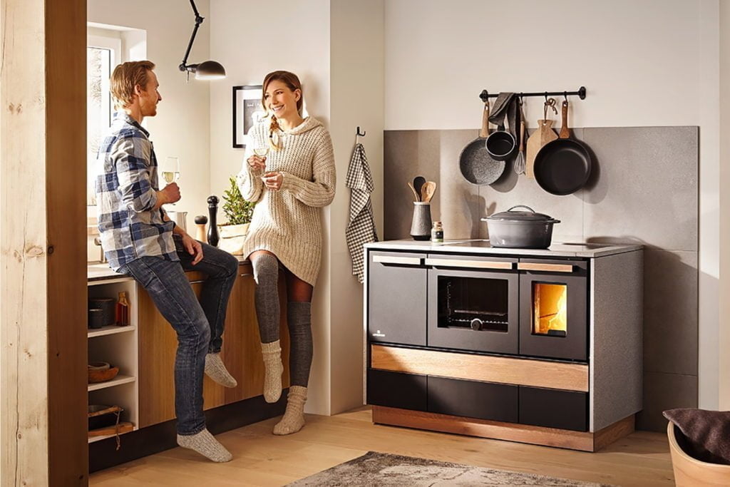 En fin vedspis från Lohberger med två människor som står bredvid den i köksmiljö.
