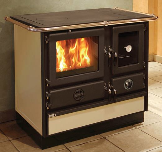 MBS Kaminer & Vedspisar: Den kompletta guiden till ett prisvärt val 4 En vedeldad kamin med ett glasfönster som visar lågorna inuti, omgiven av beige och svarta metallpaneler, står på ett klinkergolv mot en vägg.