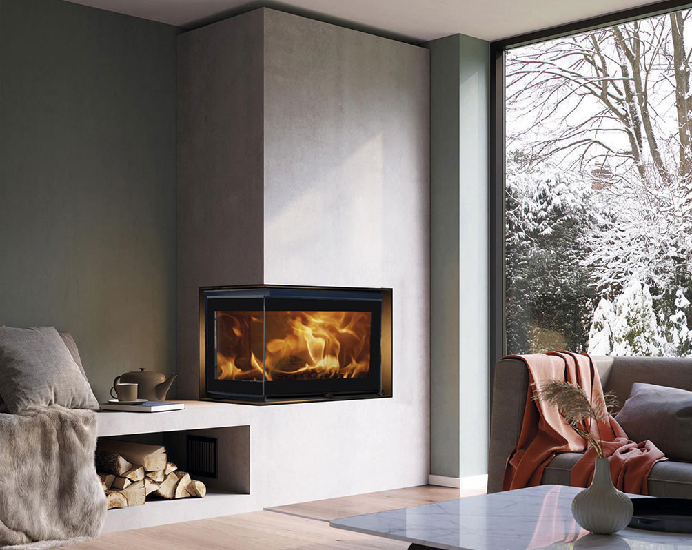 Ett modernt vardagsrum med en hörnspis som brinner starkt, ett stort fönster som visar ett snöigt utomhuslandskap, en soffa med en filt, ett soffbord med en vas och ved staplad bredvid eldstaden.