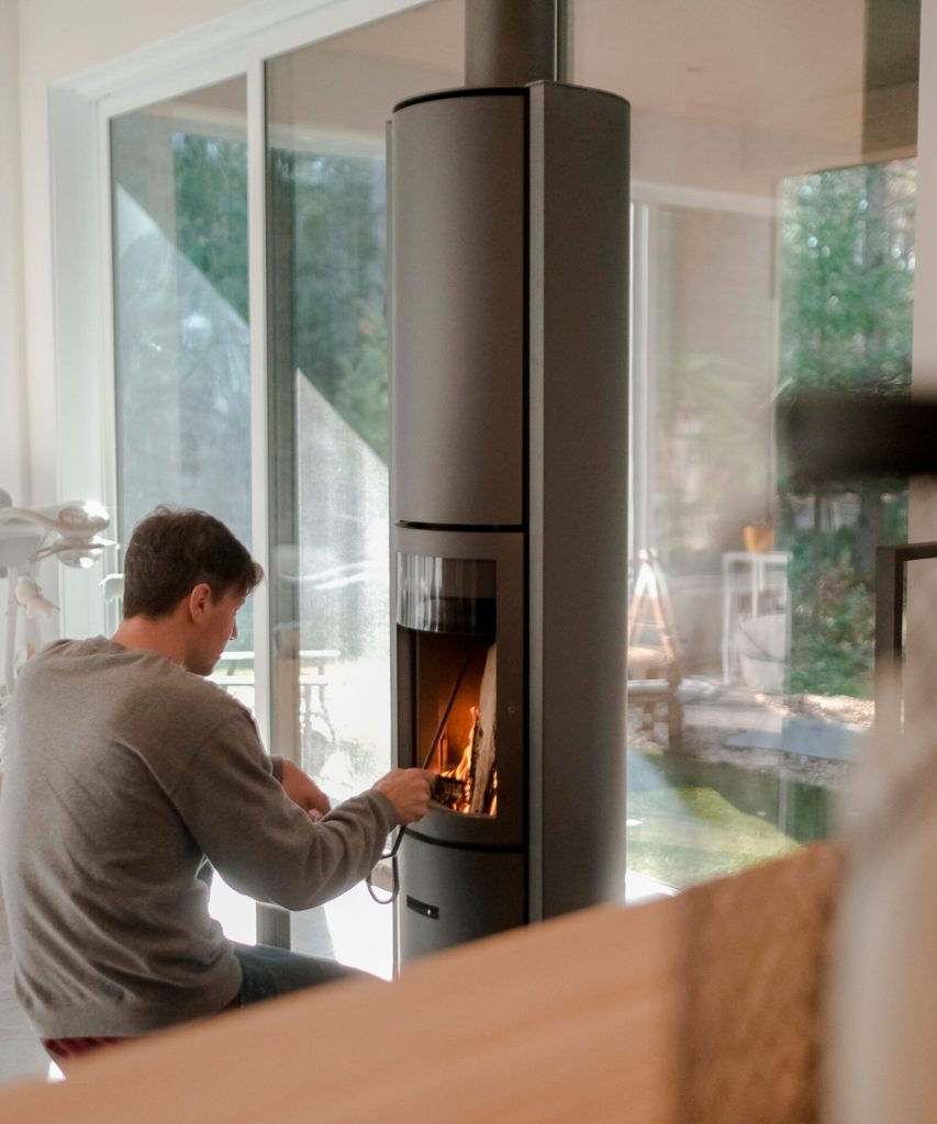 Stûv Kaminer: En guide till arkitekternas favoritmärke från Belgien 3 Man sitter framför braskaminen Stuv 30 och lägegr in ved.