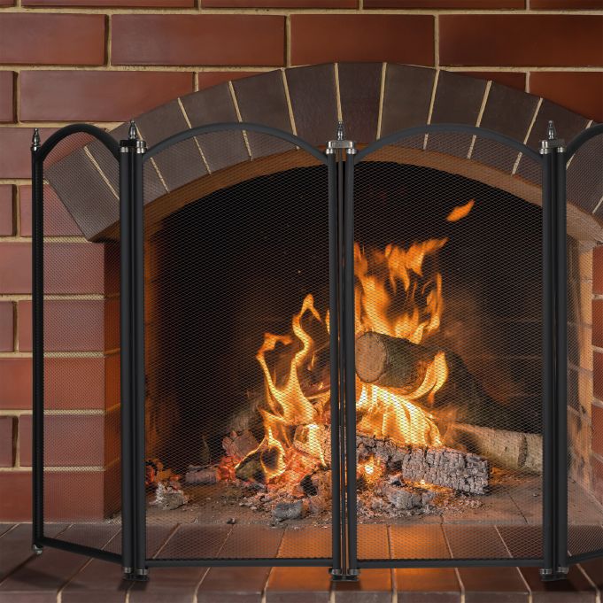 En tänd öppen spis med brinnande stockar bakom en svart metallnätskärm, placerad i en tegelvägg och härd.