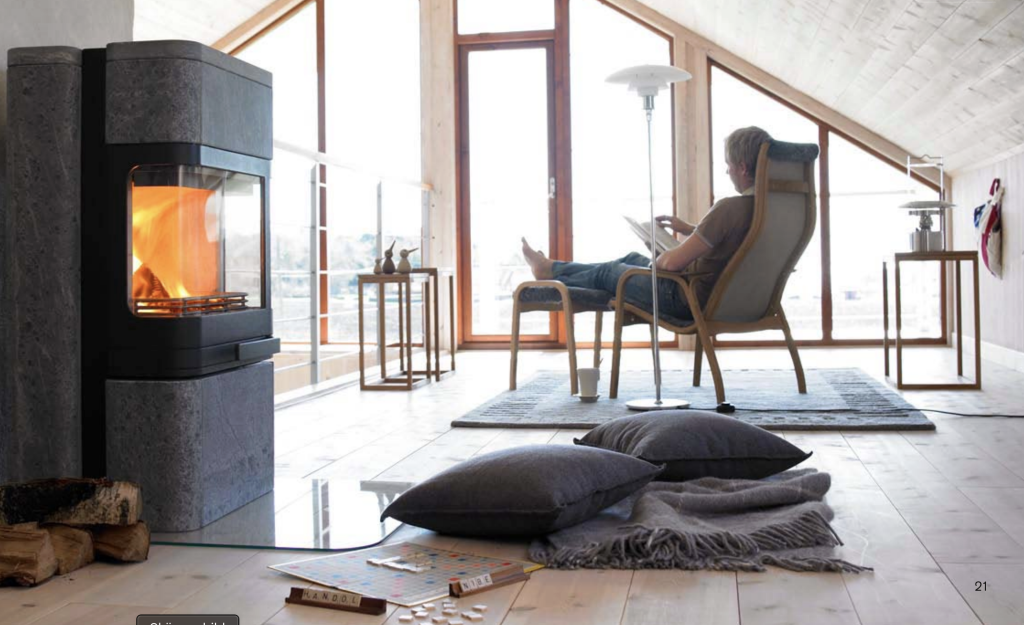 Stor täljstenskamin från Handöl med en person framför i en stol som tar det lugnt.
