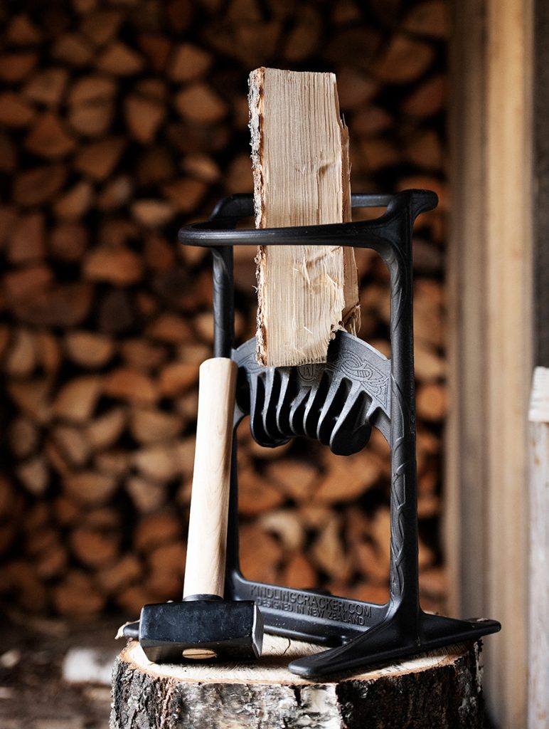 En vedklyv håller en bit ved upprätt på en trädstubbe, med en klubba vilande i närheten. Staplade vedträn är suddiga i bakgrunden.