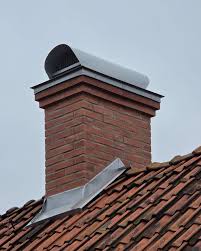 En skorsten av rött tegel med metallhätta sitter på ett sluttande tak med röda tegelpannor under en molnig himmel. Metallblecket runt skorstenens bas ger väderskydd.