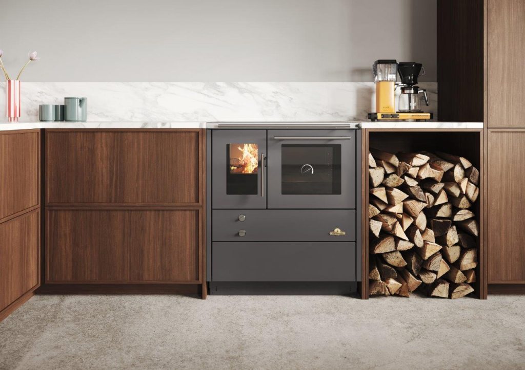 Vedspisen heimdall 790 installerad i ett modernt kök med vedfack till höger om vedspisen.